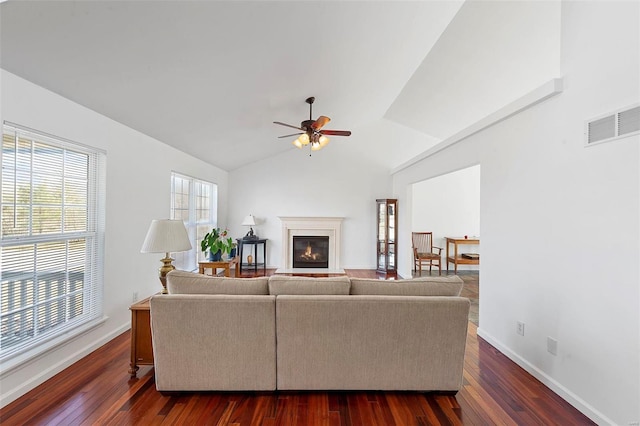 living room with visible vents, lofted ceiling, dark wood-style floors, and a glass covered fireplace