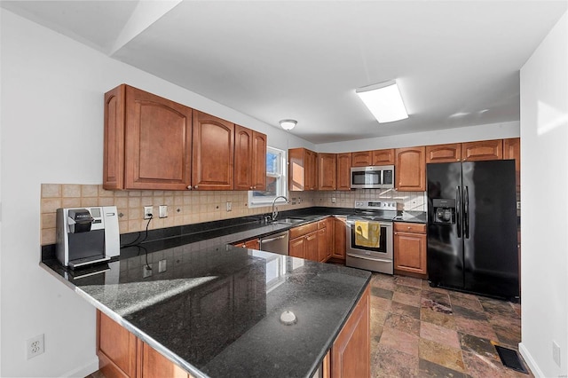 kitchen with tasteful backsplash, a peninsula, brown cabinetry, stone finish floor, and stainless steel appliances