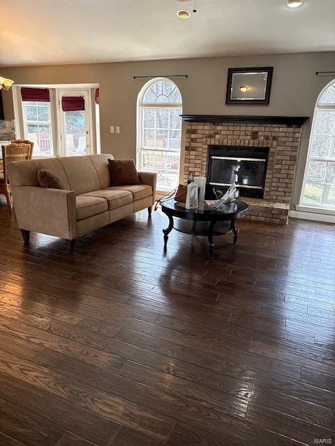 living area featuring dark wood-type flooring, a brick fireplace, and a healthy amount of sunlight