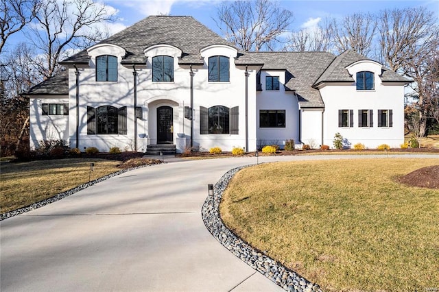 french provincial home with a front lawn, concrete driveway, and stucco siding