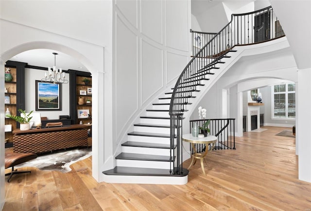 stairs featuring a notable chandelier, wood finished floors, and arched walkways