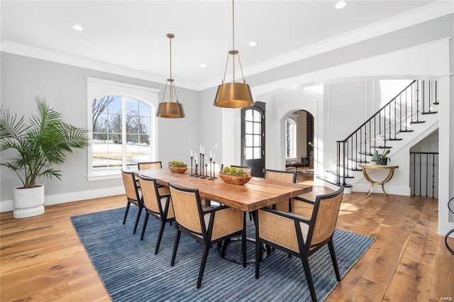 dining space featuring arched walkways, ornamental molding, baseboards, and hardwood / wood-style flooring