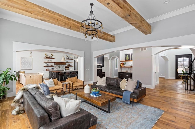 living area featuring baseboards, beam ceiling, wood finished floors, arched walkways, and a notable chandelier