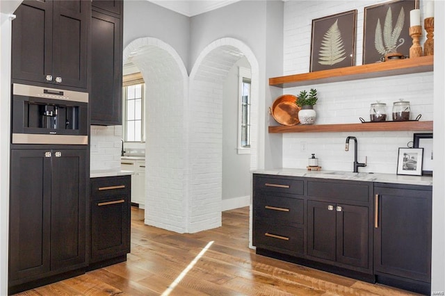 bar with light wood-style flooring, a sink, arched walkways, stainless steel oven, and decorative backsplash