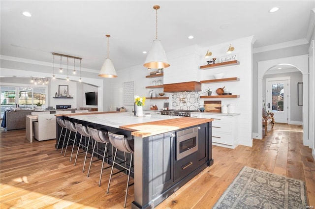 kitchen with stainless steel microwave, open floor plan, arched walkways, wood counters, and open shelves