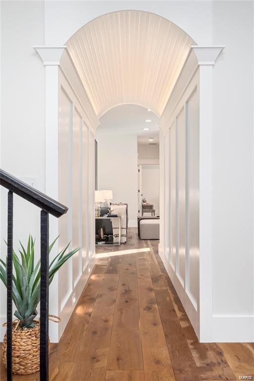 hallway with hardwood / wood-style flooring, arched walkways, and vaulted ceiling