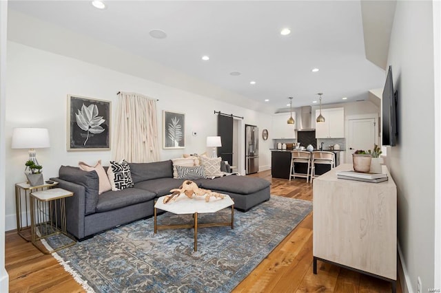 living area with recessed lighting, a barn door, baseboards, and light wood-style floors