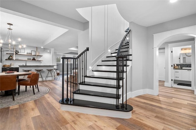 staircase with arched walkways, a notable chandelier, baseboards, and wood finished floors