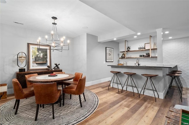 dining area with baseboards, light wood finished floors, an inviting chandelier, recessed lighting, and indoor wet bar