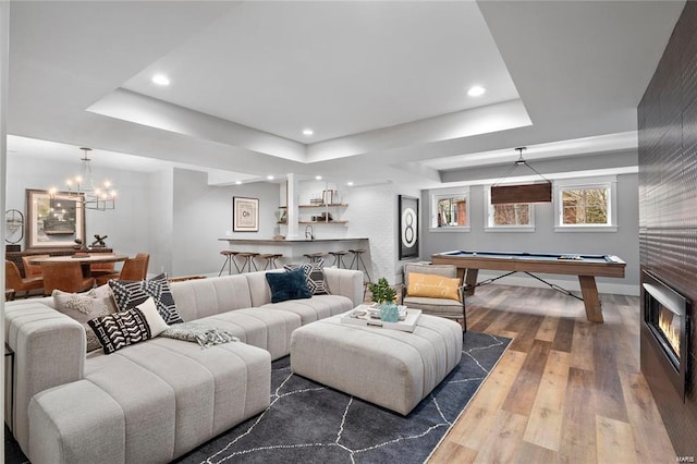 living room with a tray ceiling, recessed lighting, pool table, hardwood / wood-style flooring, and a notable chandelier