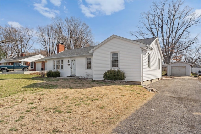 ranch-style house featuring a detached garage, a front lawn, aphalt driveway, a chimney, and an outbuilding