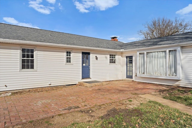 rear view of property with a patio area, entry steps, a chimney, and roof with shingles