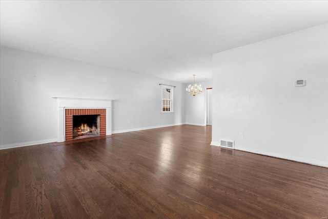 unfurnished living room with baseboards, visible vents, dark wood finished floors, a brick fireplace, and a notable chandelier