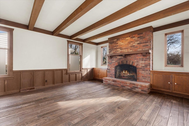 unfurnished living room featuring hardwood / wood-style floors, a fireplace, a wainscoted wall, and a wealth of natural light