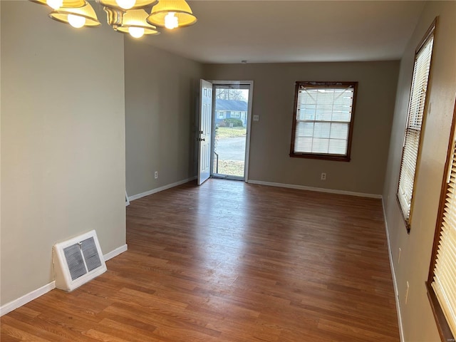 empty room with a chandelier, visible vents, baseboards, and wood finished floors