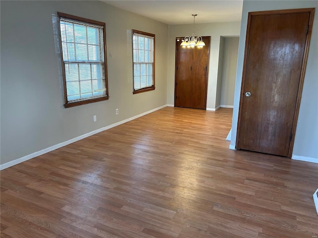 spare room featuring an inviting chandelier, wood finished floors, and baseboards