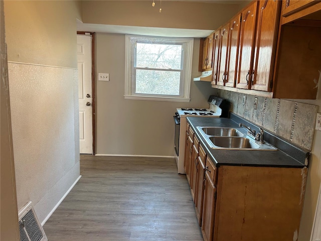 kitchen with dark countertops, visible vents, a sink, light wood-style floors, and gas range