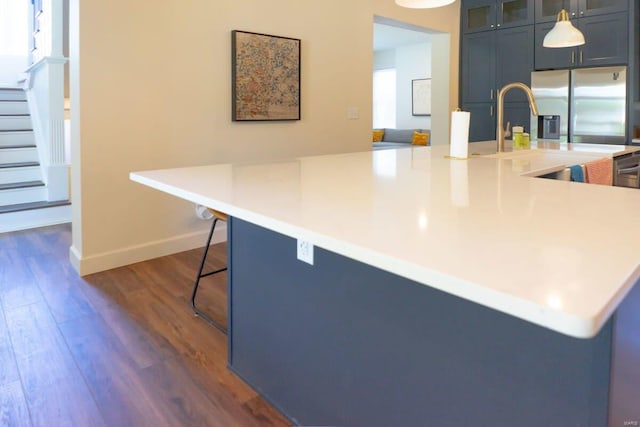 kitchen with baseboards, a breakfast bar, dark wood-style flooring, light countertops, and glass insert cabinets