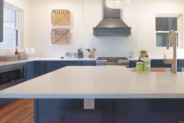 kitchen with light countertops, wall chimney range hood, blue cabinetry, and stainless steel appliances