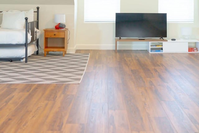 bedroom with multiple windows, wood finished floors, and baseboards