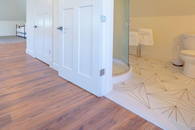 bathroom featuring baseboards, toilet, wood finished floors, and a shower stall