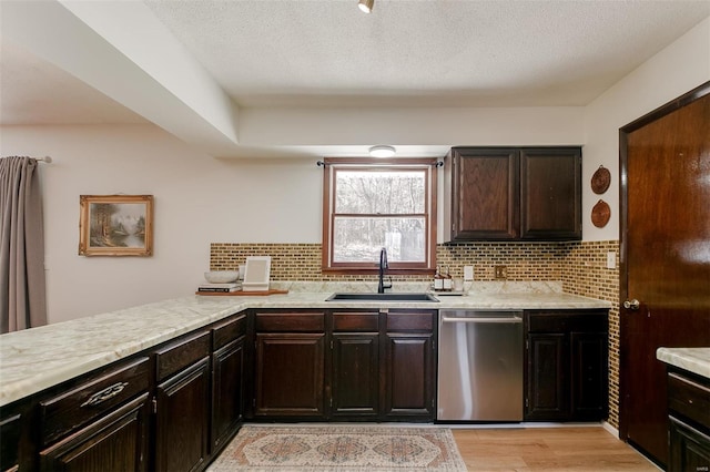 kitchen with light wood finished floors, light countertops, decorative backsplash, stainless steel dishwasher, and a sink