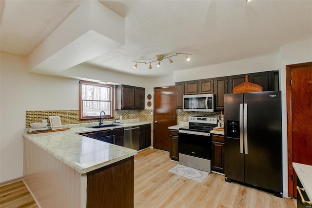 kitchen with light wood finished floors, a sink, appliances with stainless steel finishes, a peninsula, and light countertops