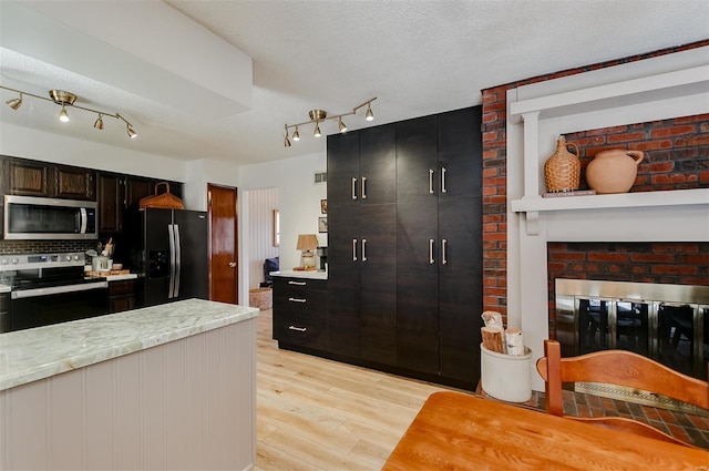 kitchen with light wood finished floors, stainless steel appliances, light countertops, a textured ceiling, and tasteful backsplash