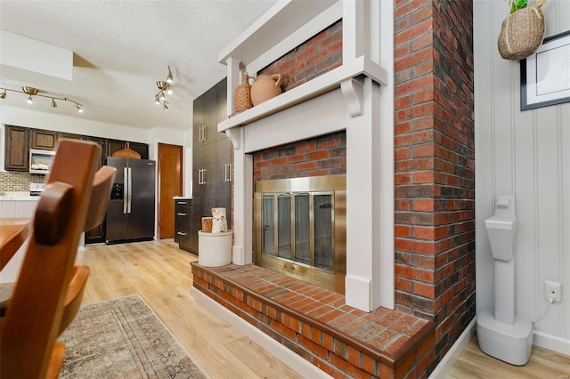 living room featuring light wood-style flooring, a brick fireplace, and a textured ceiling