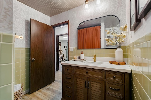 bathroom featuring vanity, wood finished floors, wallpapered walls, wainscoting, and tile walls