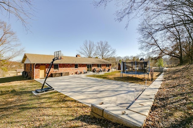 rear view of house with a yard, a chimney, a trampoline, a patio area, and brick siding