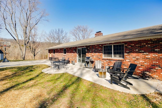 back of house with a patio, brick siding, a chimney, and a lawn