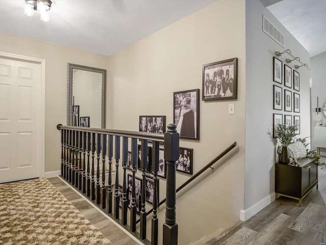 corridor with wood finished floors, an upstairs landing, visible vents, and baseboards