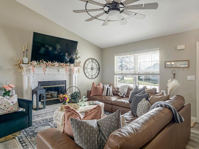 living area featuring vaulted ceiling, a brick fireplace, ceiling fan, and wood finished floors