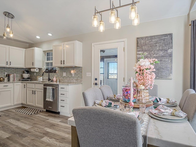 kitchen featuring a sink, decorative backsplash, vaulted ceiling, light wood-style floors, and stainless steel dishwasher