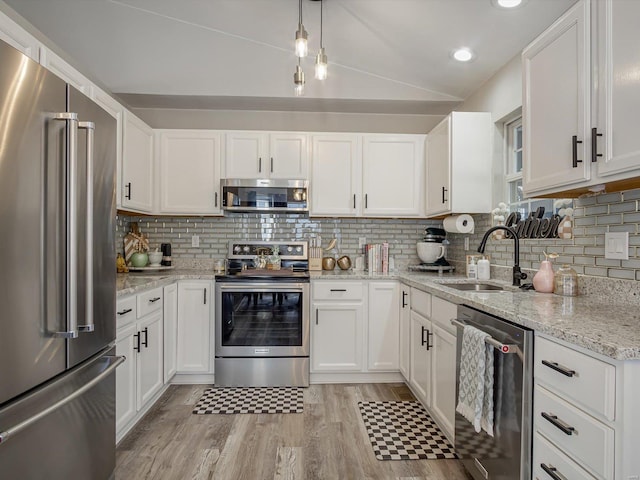 kitchen with a sink, white cabinetry, appliances with stainless steel finishes, and vaulted ceiling