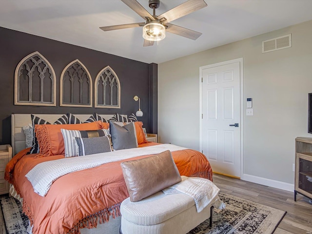 bedroom with ceiling fan, wood finished floors, visible vents, and baseboards