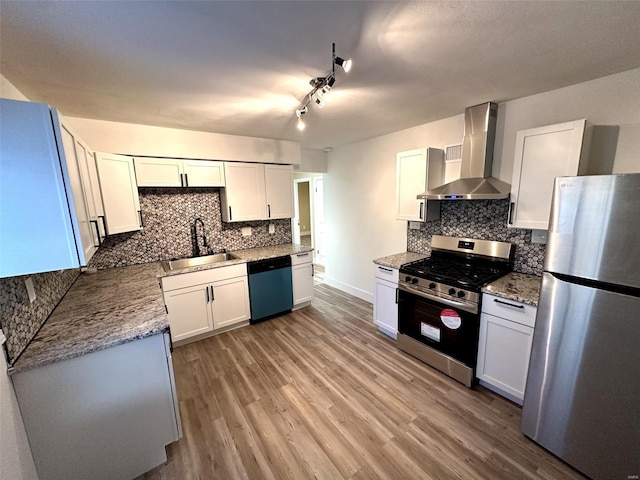 kitchen featuring wall chimney range hood, decorative backsplash, light wood-style flooring, stainless steel appliances, and a sink