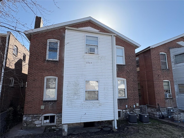 rear view of property with central air condition unit, cooling unit, brick siding, and a chimney