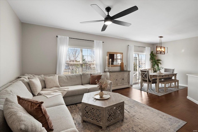 living room with dark wood finished floors, ceiling fan with notable chandelier, and baseboards