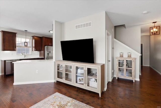 unfurnished living room featuring visible vents, a sink, an inviting chandelier, baseboards, and dark wood-style flooring