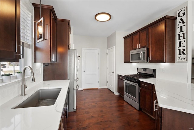 kitchen featuring light stone countertops, dark wood-style floors, a sink, appliances with stainless steel finishes, and backsplash