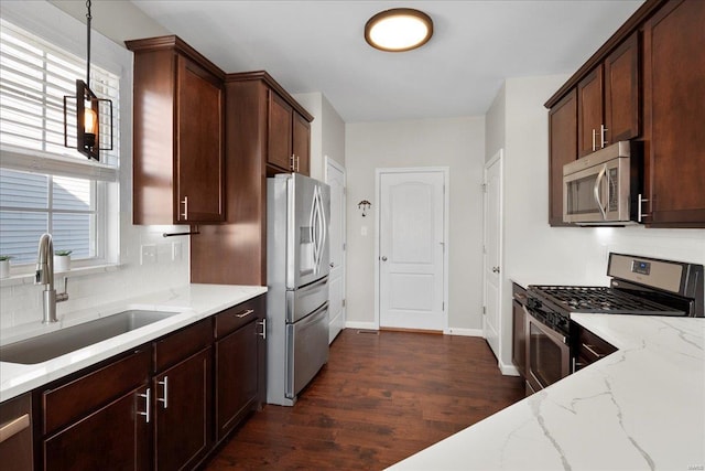 kitchen with a sink, light stone countertops, pendant lighting, appliances with stainless steel finishes, and dark wood-style flooring