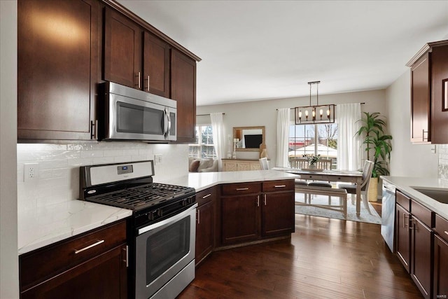 kitchen featuring tasteful backsplash, dark wood-type flooring, a peninsula, a notable chandelier, and stainless steel appliances