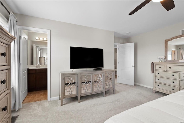 bedroom featuring visible vents, a sink, ensuite bath, baseboards, and light colored carpet