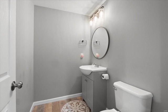 bathroom featuring baseboards, toilet, wood finished floors, and vanity