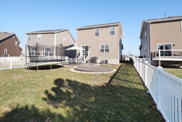 back of property with a patio area, a fenced backyard, a yard, and a trampoline