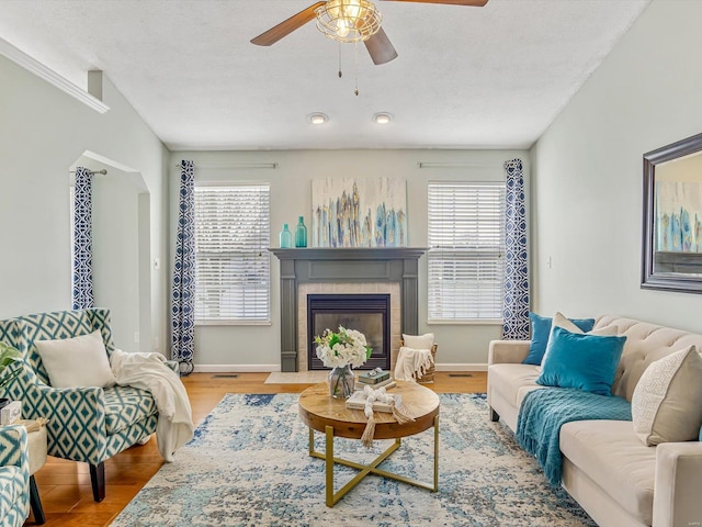 living area featuring baseboards, a textured ceiling, wood finished floors, and a tiled fireplace