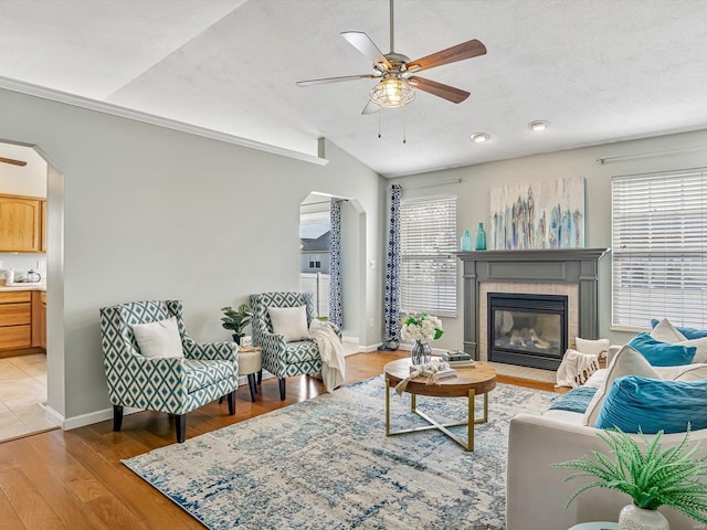 living room featuring light wood-style floors, a ceiling fan, arched walkways, and a textured ceiling