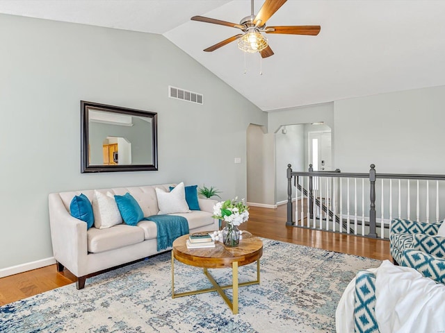 living area with visible vents, a ceiling fan, wood finished floors, baseboards, and vaulted ceiling